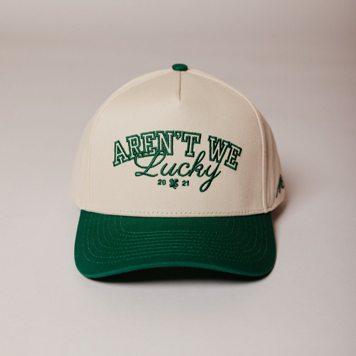A green and white baseball cap with 'AREN'T WE Lucky' embroidered on the front.