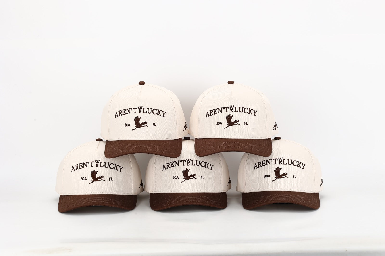 Five white caps with brown brims and 'Aren't You Lucky?' text on a white background