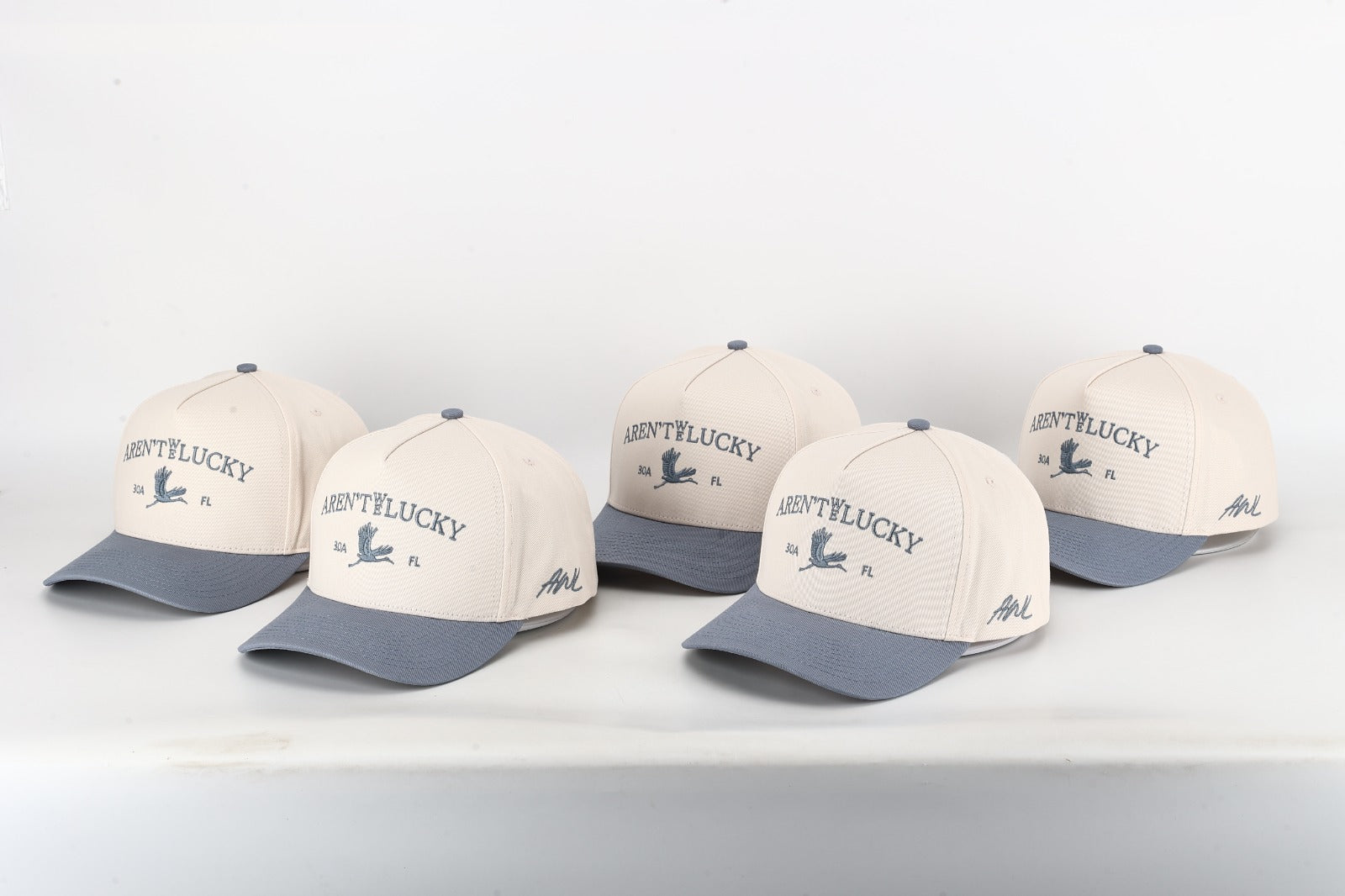 Five 'Aren't We Lucky' branded hats arranged on a white surface.