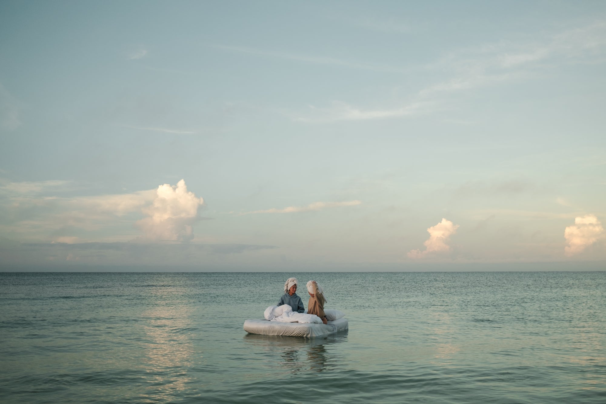 Two people on a small raft in the middle of a calm sea with a clear sky.
