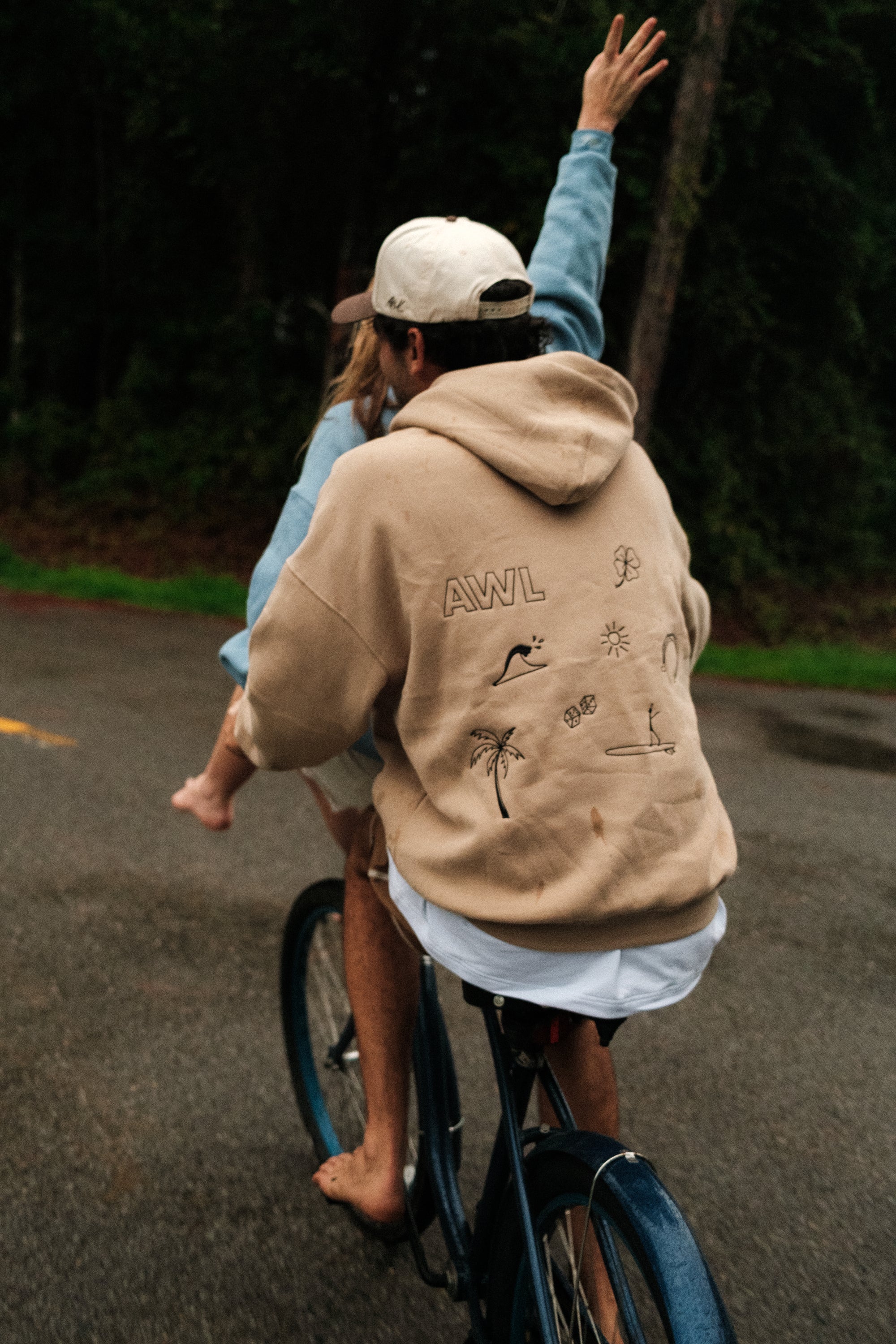 Person riding a bike with another person standing on the back, both wearing casual clothing.
