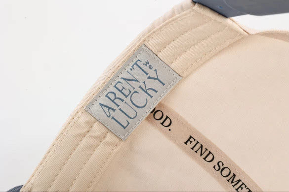 Beige cap with 'Aren't Lucky' brand label on a white background