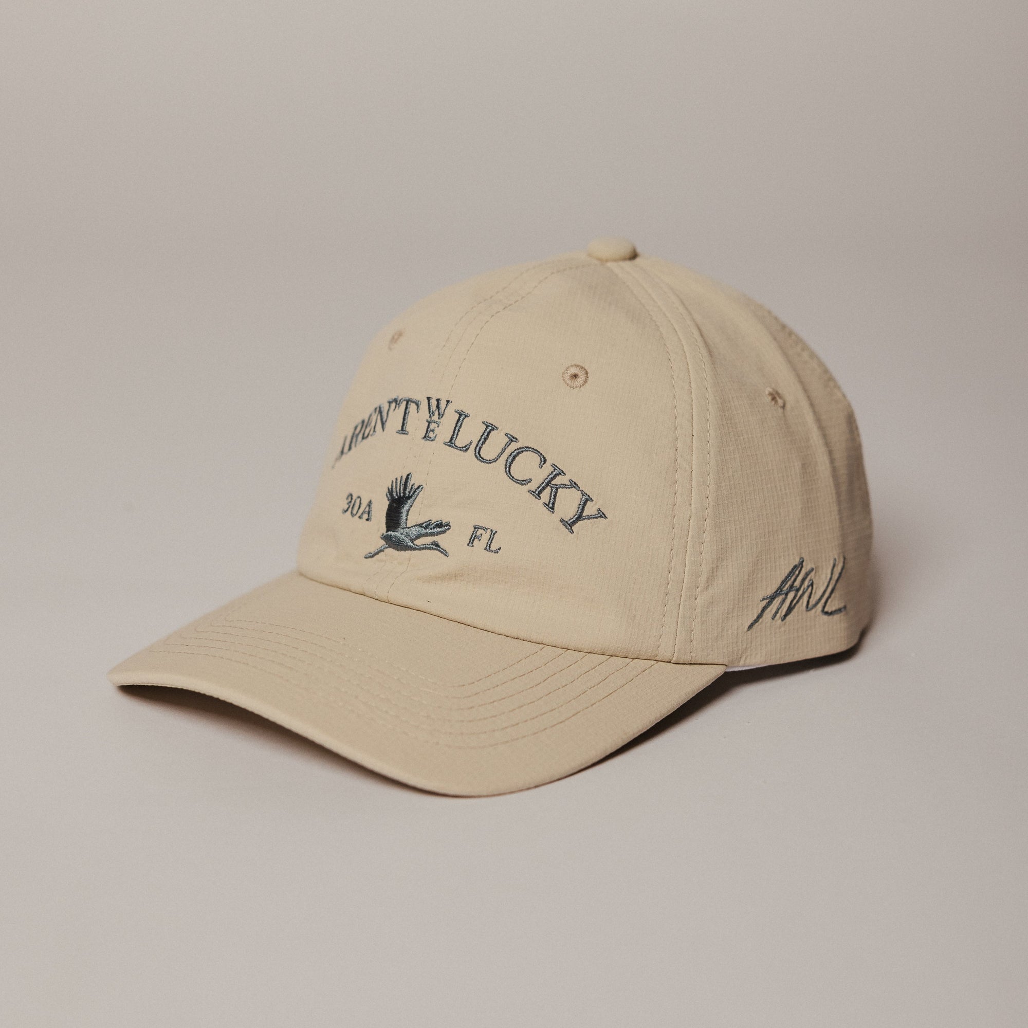 Beige Aren't We Lucky 30a Crane Dry Baseball cap with text and logo on a beige background