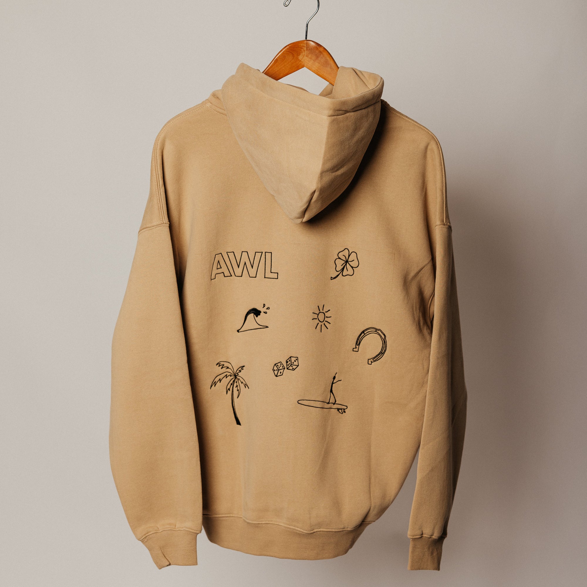 Beige hoodie with graphics and 'AWL' branding on a wooden hanger against a beige wall.