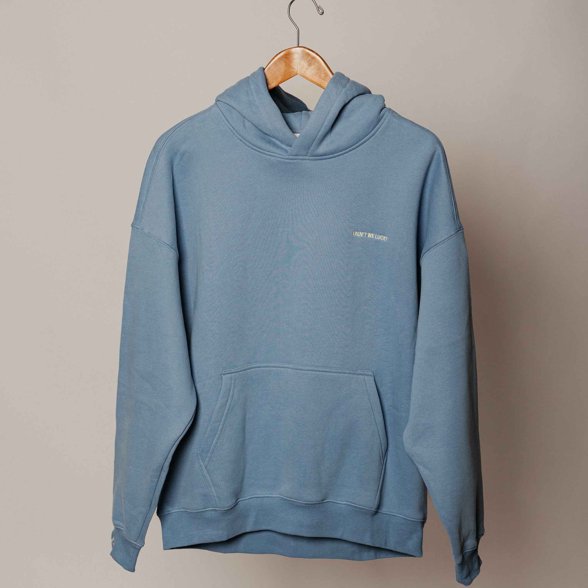Blue hoodie on a wooden hanger against a beige background