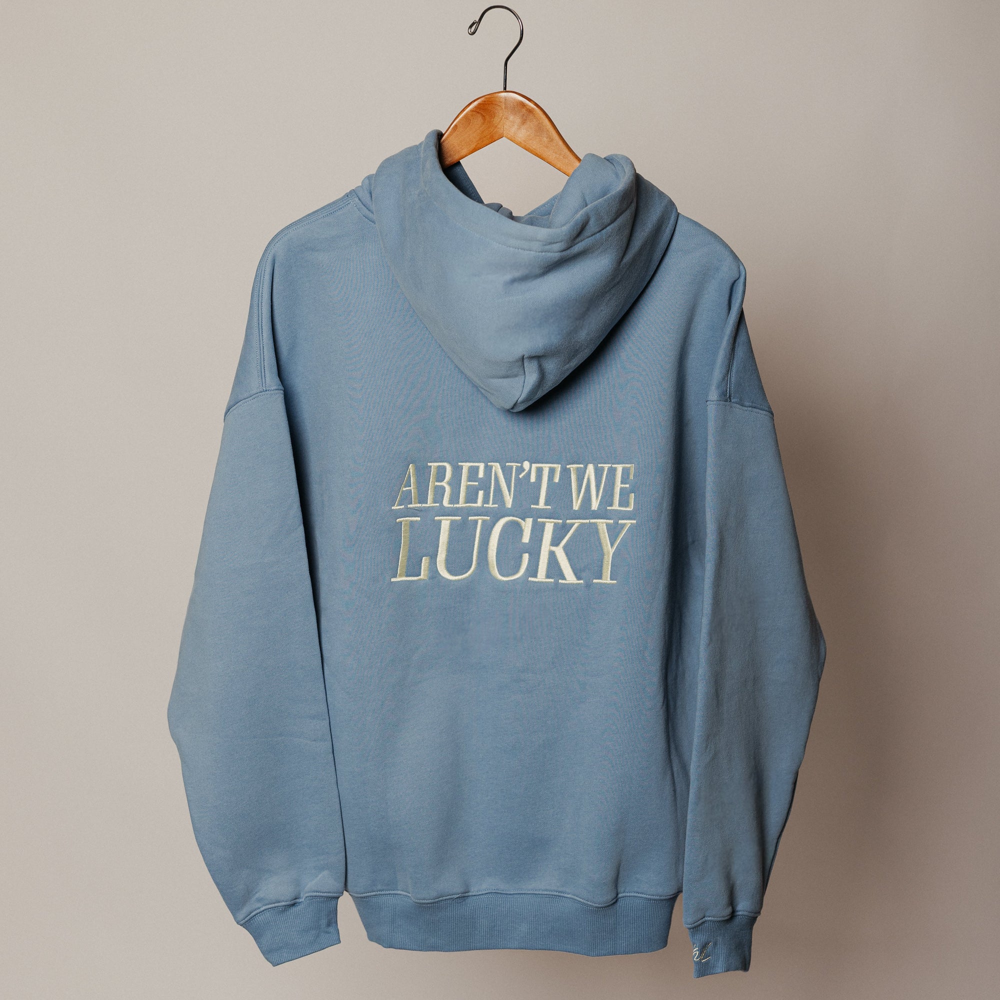 Blue hoodie with 'AREN'T WE LUCKY?' text on a beige background